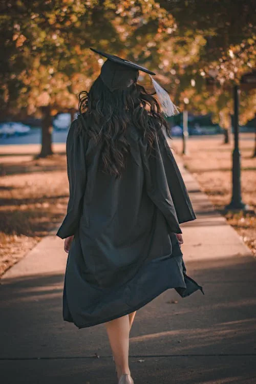 Girl in cap and gown, walking down pathway after graduating