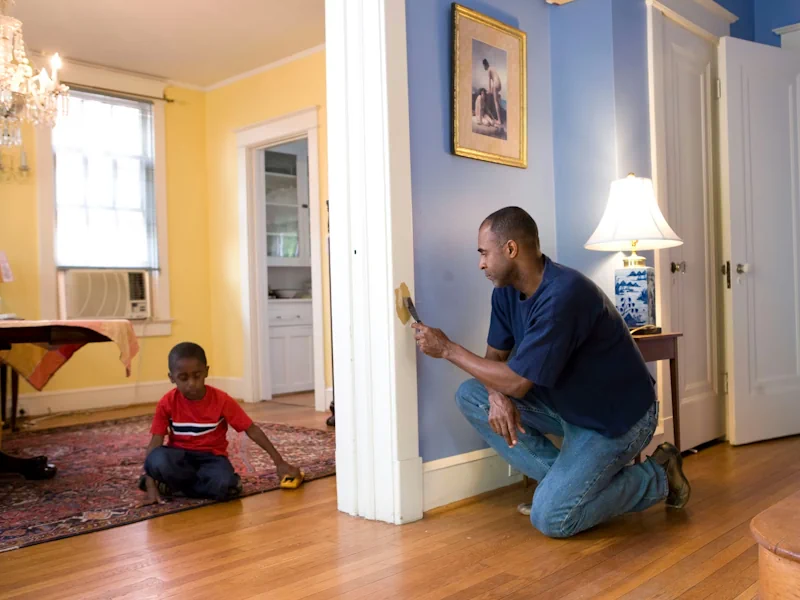 Homeowner doing minor repair work on some door molding while his son plays in the adjacent dining room