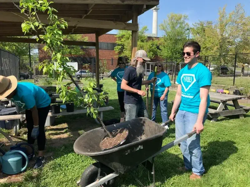 Trenton Community Corps member transporting a sapling tree in a wheel barrow.